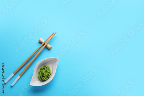 Bowl with swirl of wasabi paste and chopsticks on light blue background, flat lay. Space for text