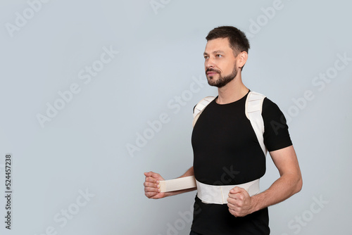 Fotografie Handsome man with orthopedic corset on grey background, space for text