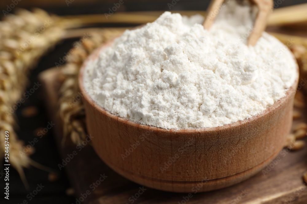 Wheat flour in bowl, spikes and grains on wooden board, closeup Wheat flour in bowl, spikes and grains on wooden board, closeup