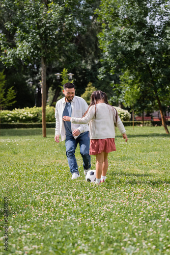 Positive asian dad playing soccer with daughter in park.