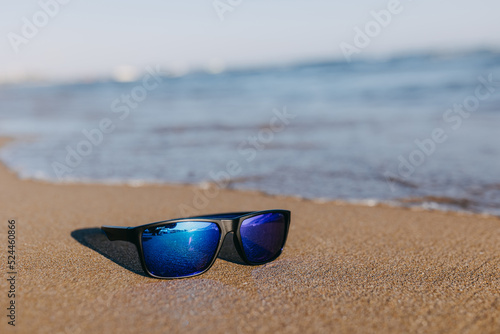 Blue sunglasses in water on a seashore sand