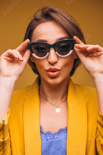 Portrait of woman in yellow suit wearing black and white sunglasses isolated in studio