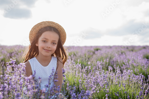 brunette girl in straw hat smiling at camera in lavender field on summer day.