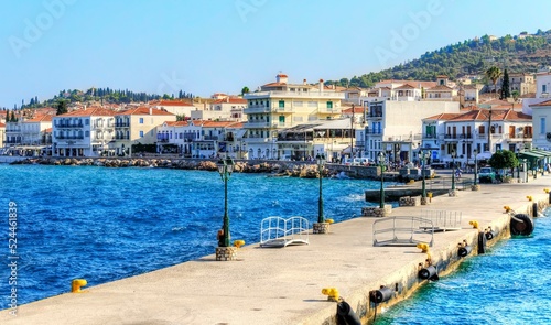 A view of the port skyline of the beautiful Greek Island, Spetses, the pier leading to the city and some of the local architecture.
