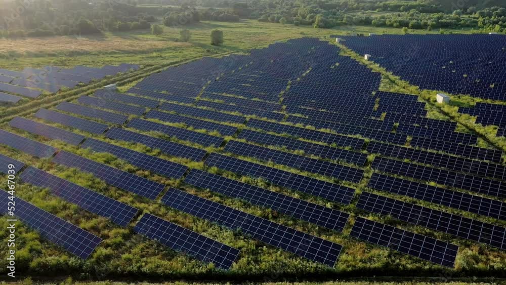 Aerial Top view on Solar Power Station in Green Field on Sunny day. Drone fly over Solar Farm. Lot of Solar Panels Stand in Row for Power Production. Renewable green energy. Aerial Top view on Solar Power Station in Green Field on Sunny day. Drone fly over Solar Farm. Lot of Solar Panels Stand in Row for Power Production. Renewable green energy.