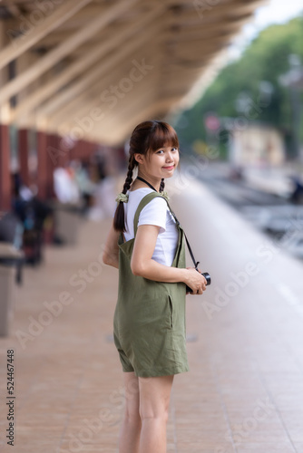 Portrait Young asian woman smiling tourist Traveler girl walking and with a holding the camera waits train travel journey is taken in railway platform Thailand, summer relax vacation Concept. © Thinapob