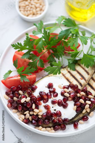 Grilled slices of aubergine served with pomegranate seeds, pine nuts, yogurt, red tomatoes and parsley, closeup, vertical shot