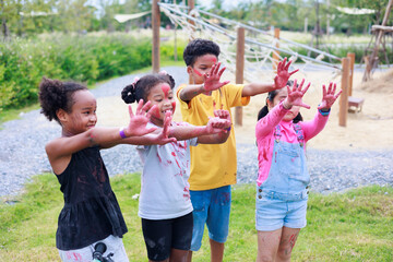 Affican child and Asian girl show colorful hand. Diverse happiness kid group playing in playground at summer camp learning