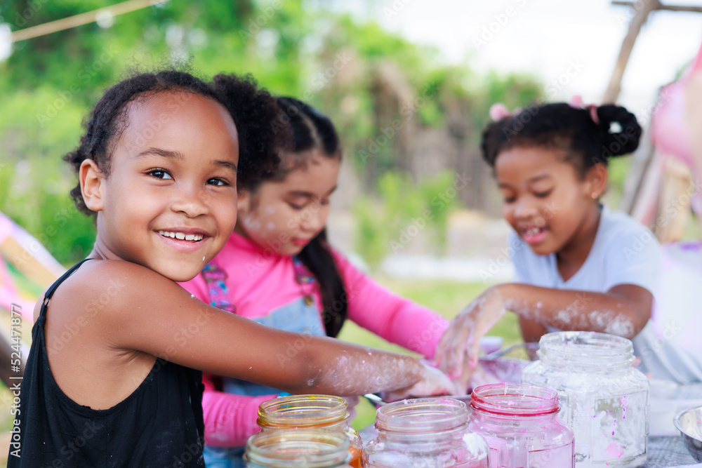 © NVB Stocker - Lovely Asian and smiling African girls making and play colorful dough together at playground, summer camp learning