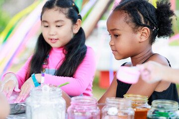 Lovely Asian and African girls playing dough together at playground, summer camp learning