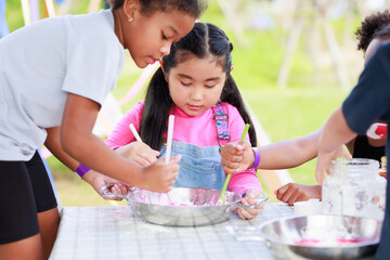 Lovely Asian and African girls playing dough together at playground, summer camp learning