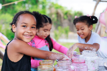Lovely Asian and smiling African girls making and play colorful dough together at playground, summer camp learning