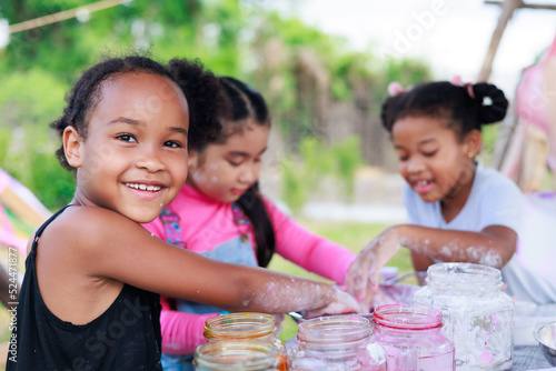 Lovely Asian and smiling African girls making and play colorful dough together at playground, summer camp learning