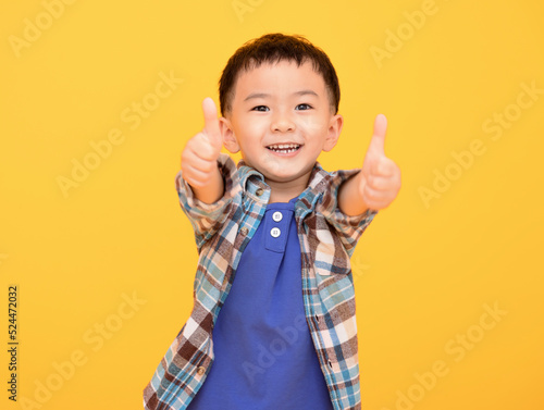 happy little boy in front of yellow background and showing thumbs up