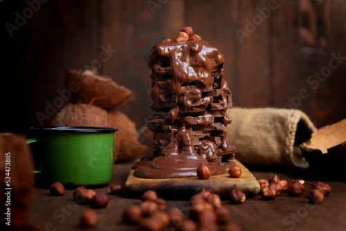 Hot chocolate in the mug and stack of chocolate bars with melted chocolate cream dripping over it