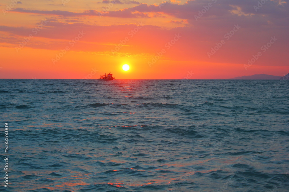 Pink sunset over the sea with clouds and a ship on the horizon