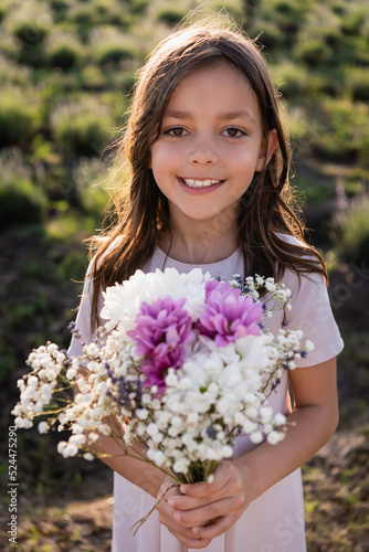 cheerful girl with floral bouquet smiling at camera in blurred field. © LIGHTFIELD STUDIOS