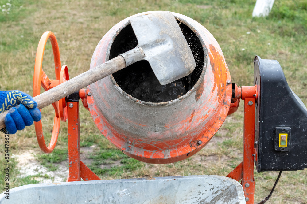 A worker shovels sand into a concrete mixer, preparing cement mortar A worker shovels sand into a concrete mixer, preparing cement mortar