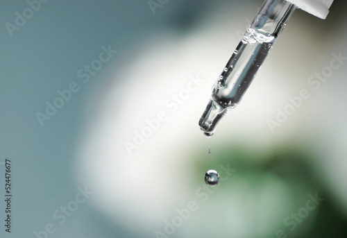 Pipette with serum, hyaluronic acid close up on blue background. Drop falling from pipet. Cosmetics, healthcare concept. Essential oill, retinol. Beauty product presentation, front view, macro