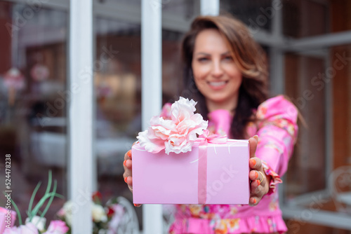 Smiling glorious brown-haired woman showing holiday present wrapped in pink box on birthday  Valentines Day or 8 march 