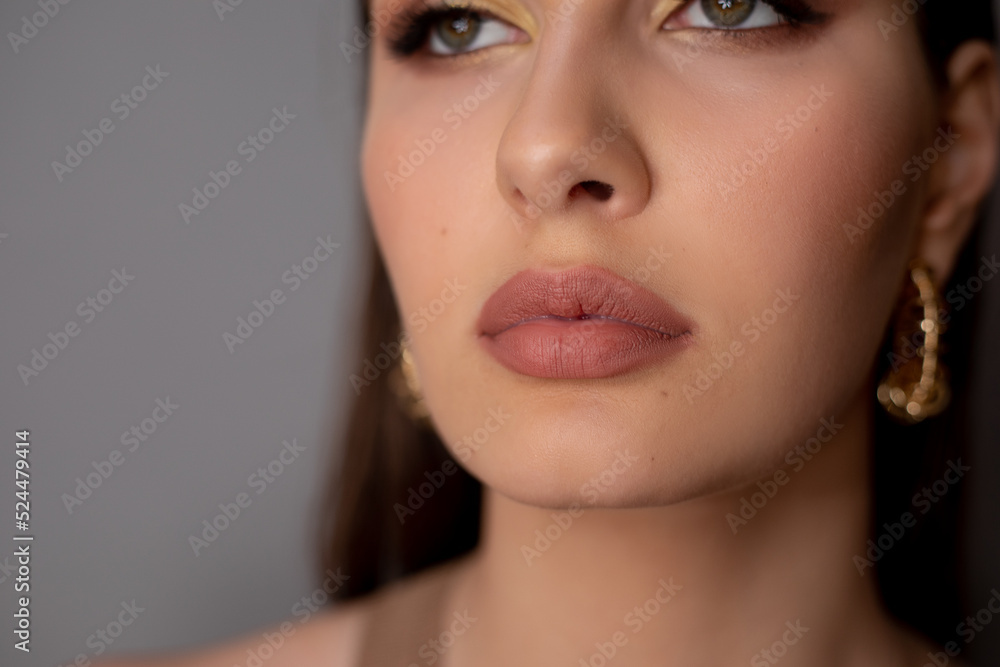 Close-up of young mysterious green-eyed woman with long dark hair, bright golden make-up, pink lips, golden earrings. Close-up of young mysterious green-eyed woman with long dark hair, bright golden make-up, pink lips, golden earrings.