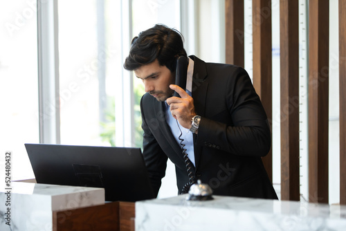 Handsome male receptionist is talking to a tourist who is making a online booking over the phone