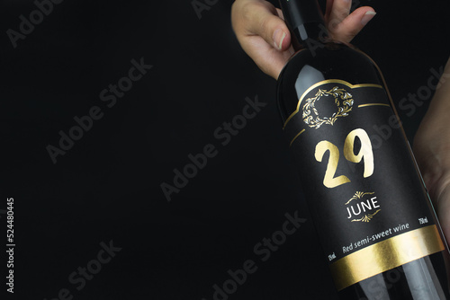 June 29th. Day 29 of month, Calendar date. Hands hold bottle of red wine with a calendar date on label. Summer month, day of the year concept.