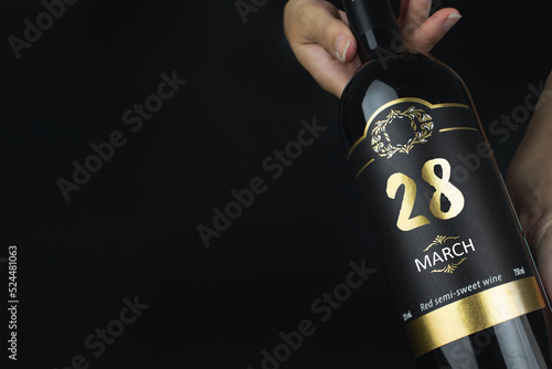 March 28th. Day 28 of month, Calendar date. Hands hold bottle of red wine with a calendar date on label. Spring month, day of the year concept.