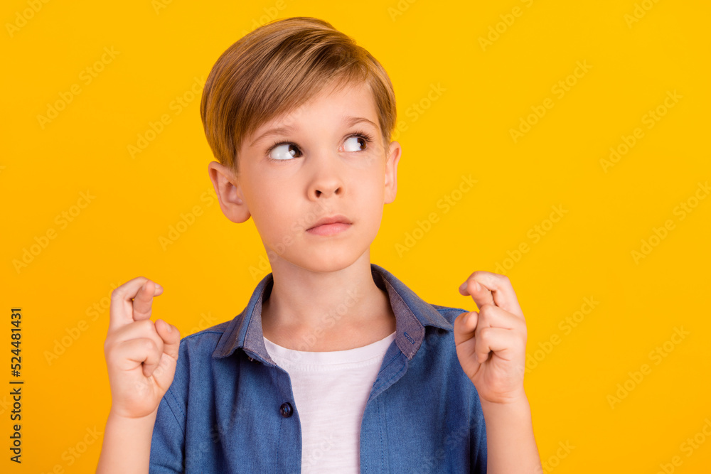 Portrait of schoolboy crossed fingers look interested empty space isolated on yellow color background Portrait of schoolboy crossed fingers look interested empty space isolated on yellow color background