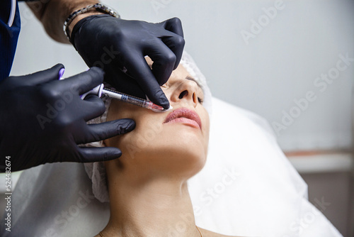 The doctor cosmetologist in black gloves makes Lip augmentation procedure of a european woman in a beauty salon. 