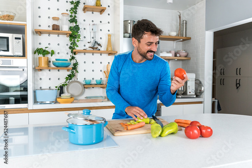 Young sporty man cutting and cooking fresh natural vegetables at kitchen and cooking for healthy lunch. Self care yoga nutritionist having healthy meal after workout.