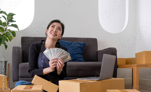 Young woman freelancer working and holding money with cardboard box  at home - SME business online and delivery concept