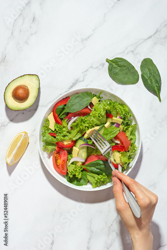Vegetable salad with avocado in a white plate on a gray background