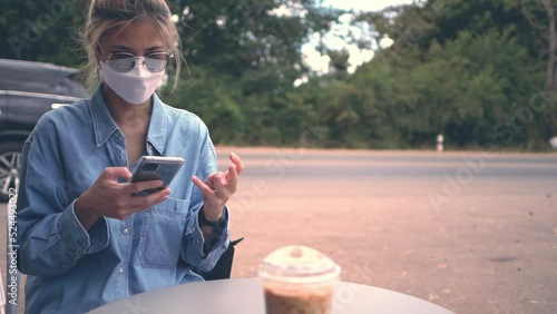 Asian woman using mobile with coffee while sitting in an outdoor cafe on the street.