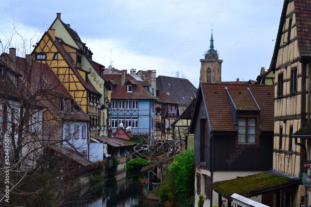 Fototapeta premium Colmar, France - December 27th 2021: View of the old streets during winter, at Christmas time. Focus on a small river going throught the city. 