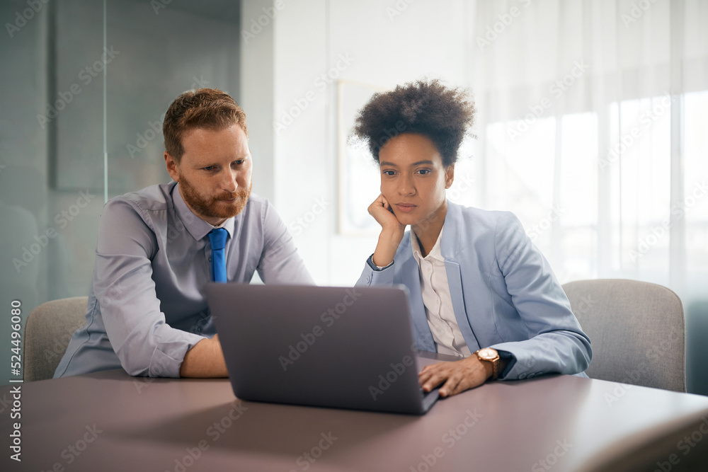 Fototapeta premium Pensive coworkers read an e-mail on laptop while working in office.