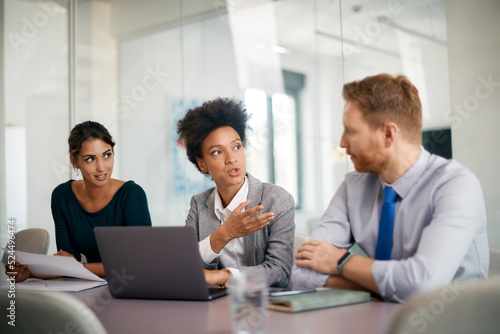 Black CEO using laptop while talking to her colleagues during business meeting in office.