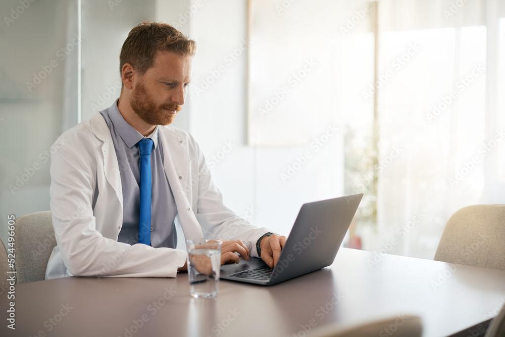 Mid adult doctor works on laptop at his office.