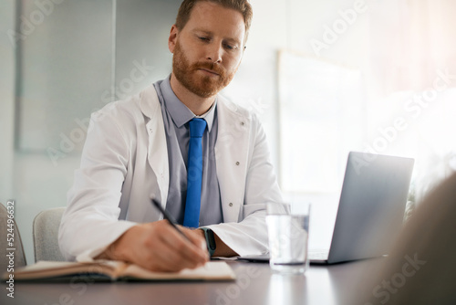 Doctor taking notes while working on computer at his office.