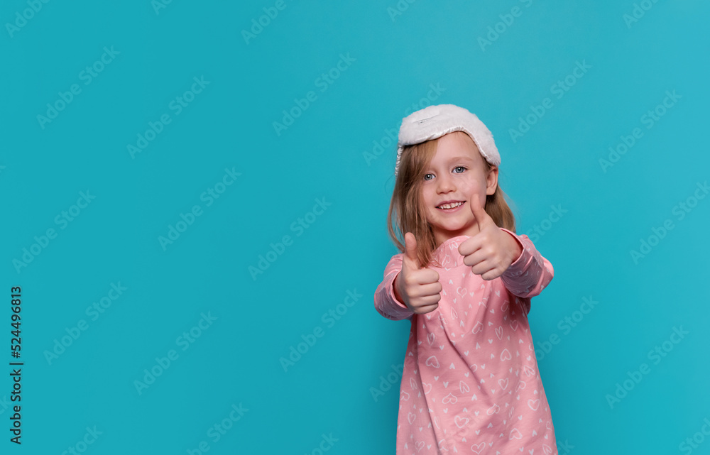 a little girl in pajamas and a sleep mask shows a like on a blue background, copy space a little girl in pajamas and a sleep mask shows a like on a blue background, copy space