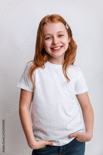 Redhead smiling little girl model posing in white t-shirt on grey background