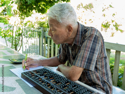 Old man writing and using wooden Chinese abacus photo