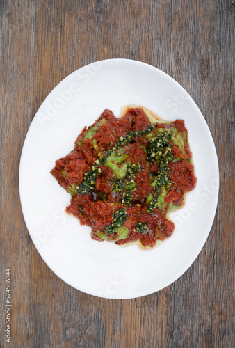 Pasta. Top view of spinach ravioli with tomato sauce and pesto, in a white dish.