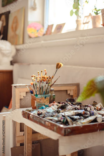 Painting process in artist's workshop, close up photo of brushes and tubes of paint