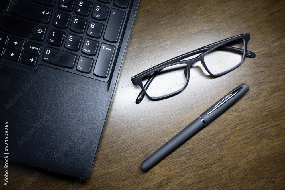 The glasses with the laptop and the pen on the brown wooden working table. The glasses with the laptop and the pen on the brown wooden working table.