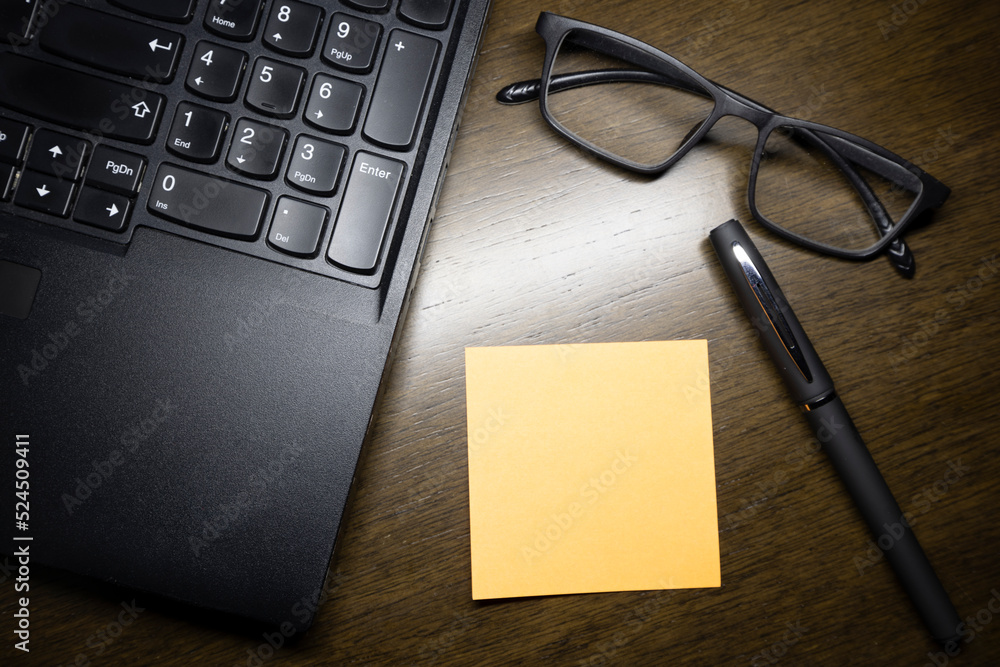 The glasses with the laptop , paper note and the pen on the brown wooden working table. The glasses with the laptop , paper note and the pen on the brown wooden working table.