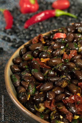 Macro close up of black beans with dried tomatoes and red Cayenne chili peppers in a brown dish.