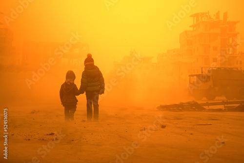 Two homeless little girl walking in ruined city photo