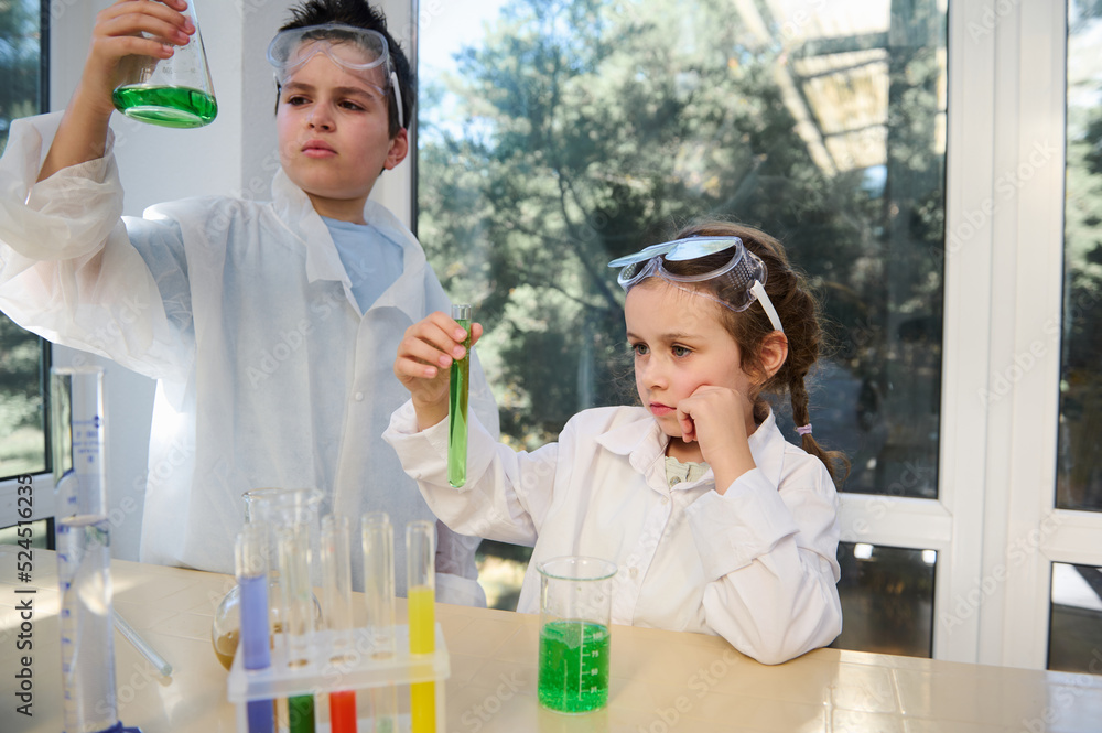 Serious students standing at the table and observing the chemical reaction going on in flat bottomed flask and test tubes. Miracles of chemistry. Learning new subject in the new academic year semester Serious students standing at the table and observing the chemical reaction going on in flat bottomed flask and test tubes. Miracles of chemistry. Learning new subject in the new academic year semester