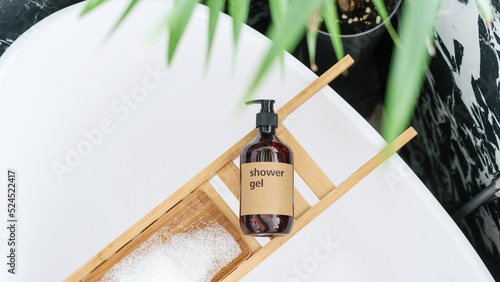 shower gel in bottle on wooden tray on tub in bathroom